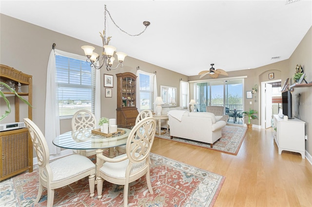 dining space with ceiling fan with notable chandelier, light hardwood / wood-style floors, and a wealth of natural light