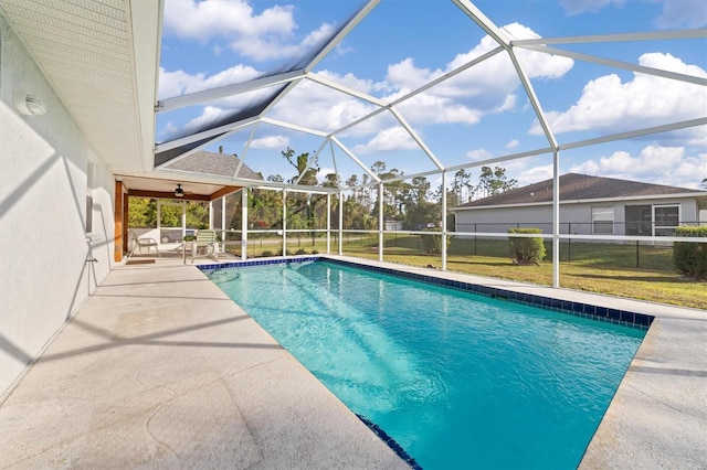 view of pool with a lawn, glass enclosure, ceiling fan, and a patio