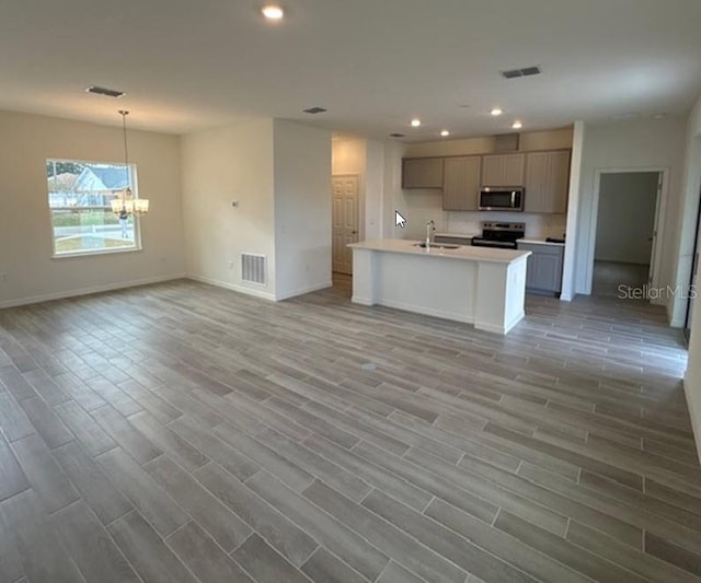 kitchen with a kitchen island with sink, an inviting chandelier, sink, appliances with stainless steel finishes, and light hardwood / wood-style floors