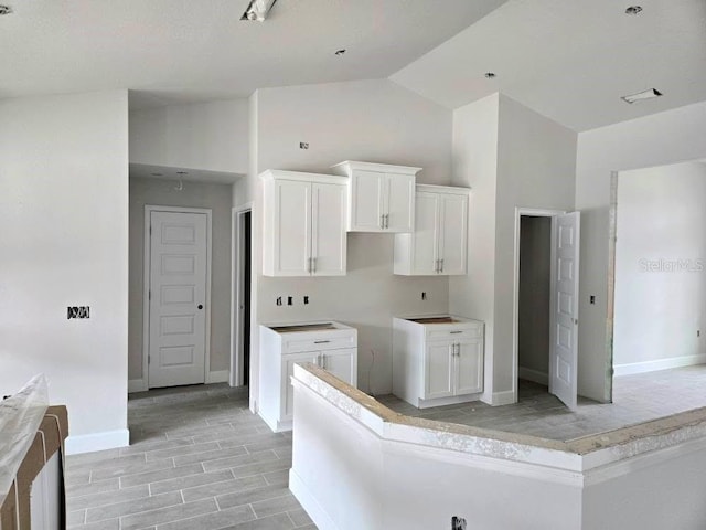 kitchen featuring high vaulted ceiling, wood finish floors, white cabinetry, and baseboards