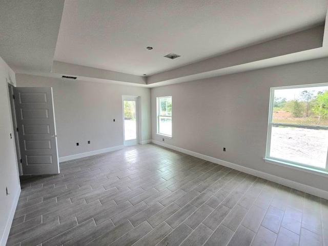 spare room featuring a tray ceiling, wood finished floors, and baseboards