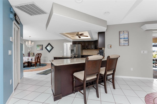 kitchen with a breakfast bar, dark brown cabinets, ceiling fan with notable chandelier, a raised ceiling, and stainless steel fridge with ice dispenser