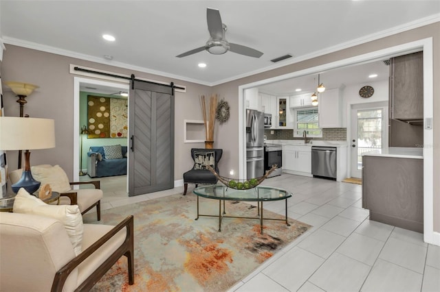 living room with ceiling fan, sink, a barn door, crown molding, and light tile patterned flooring