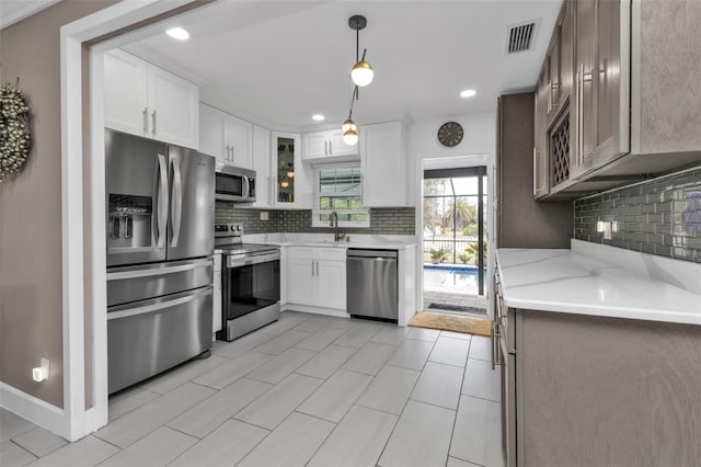 kitchen with backsplash, sink, hanging light fixtures, white cabinetry, and stainless steel appliances