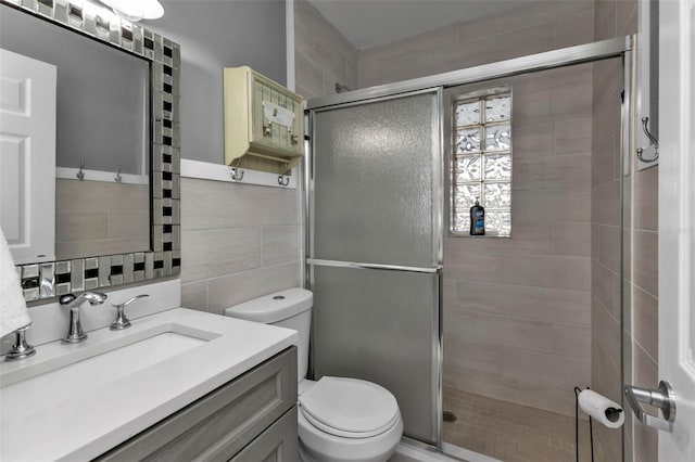 bathroom featuring vanity, a shower with shower door, tile walls, and toilet