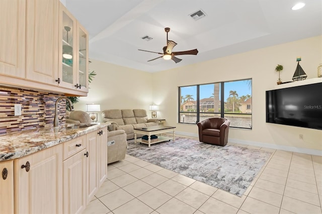 living room featuring a raised ceiling, ceiling fan, sink, and light tile patterned floors