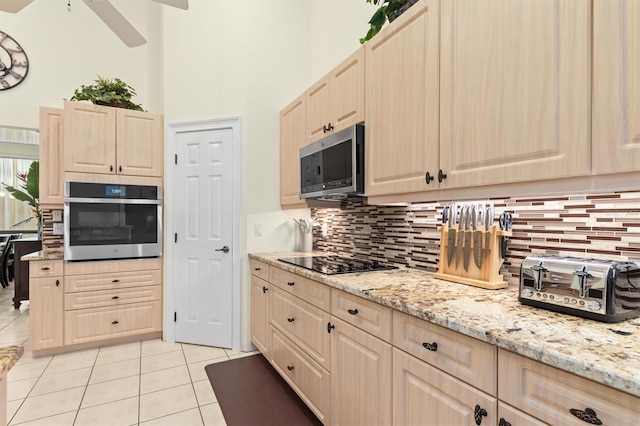 kitchen featuring light tile patterned floors, stainless steel appliances, backsplash, a towering ceiling, and light brown cabinetry