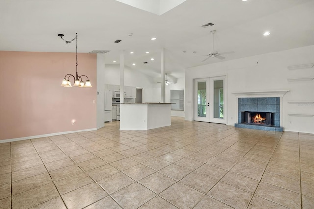 unfurnished living room featuring light tile patterned floors, ceiling fan with notable chandelier, vaulted ceiling, and a tiled fireplace