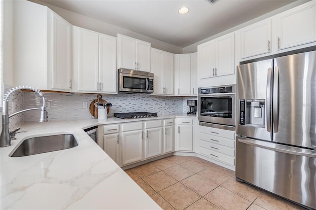 kitchen featuring white cabinets, sink, light tile patterned floors, light stone counters, and stainless steel appliances