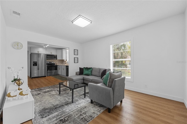 living area with baseboards, visible vents, light wood-type flooring, and a textured ceiling