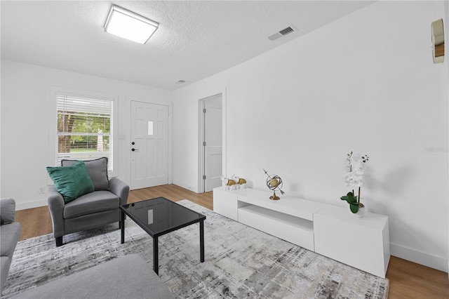 living area featuring visible vents, a textured ceiling, baseboards, and wood finished floors