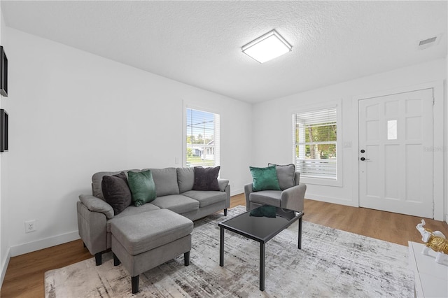 living room with baseboards, wood finished floors, visible vents, and a textured ceiling