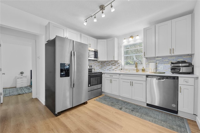 kitchen with a sink, stainless steel appliances, light countertops, light wood-style floors, and tasteful backsplash