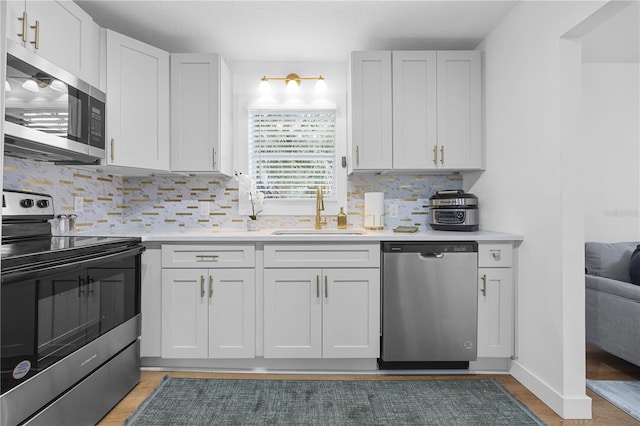 kitchen with a sink, decorative backsplash, light countertops, stainless steel appliances, and white cabinetry