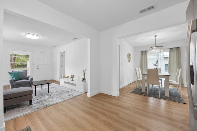 interior space featuring light wood-style flooring, a notable chandelier, baseboards, and visible vents