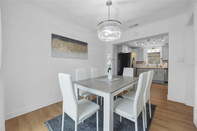 dining space featuring visible vents, baseboards, light wood-style floors, and a notable chandelier