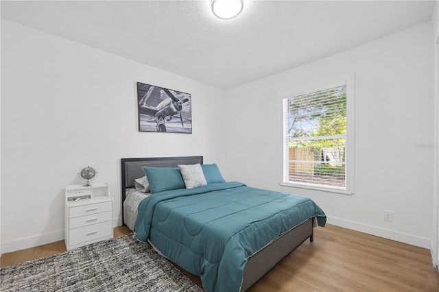 bedroom with a textured ceiling, baseboards, and wood finished floors