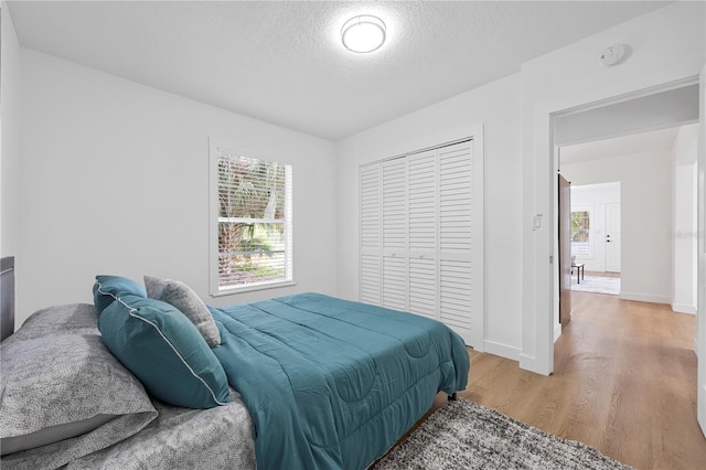 bedroom with a closet, a textured ceiling, baseboards, and wood finished floors