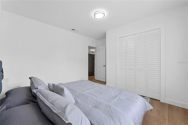 bedroom with wood finished floors, visible vents, a closet, and baseboards