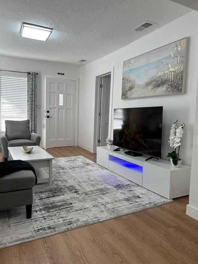 living room featuring baseboards, wood finished floors, visible vents, and a textured ceiling