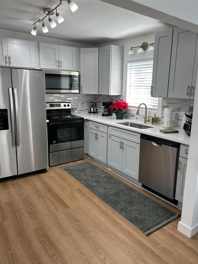 kitchen featuring a sink, stainless steel appliances, light wood finished floors, and light countertops