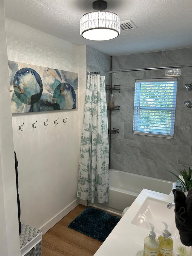 bathroom featuring baseboards, wood finished floors, shower / bath combo with shower curtain, and a textured ceiling