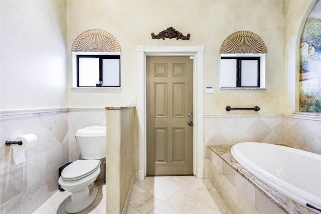 bathroom with tile patterned flooring, a relaxing tiled tub, tile walls, and toilet