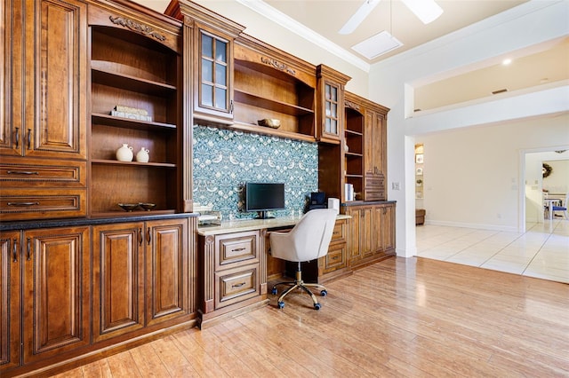 office featuring built in desk, light wood-type flooring, ceiling fan, and ornamental molding