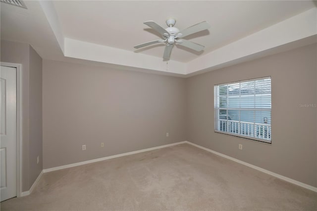 empty room with light colored carpet, ceiling fan, and a tray ceiling