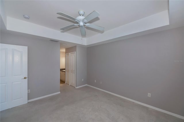 unfurnished bedroom featuring ceiling fan, a closet, light colored carpet, and a tray ceiling