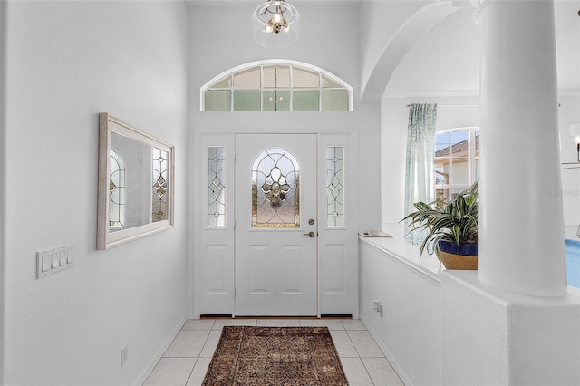 entrance foyer featuring light tile patterned floors, arched walkways, baseboards, and a towering ceiling