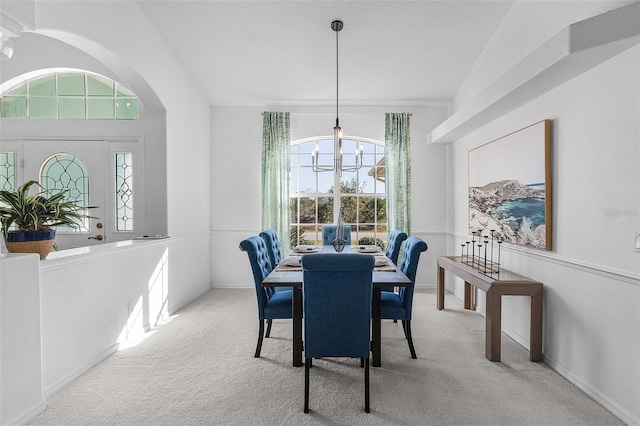 carpeted dining room with an inviting chandelier and vaulted ceiling