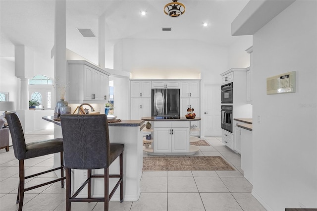 kitchen with a kitchen breakfast bar, black appliances, high vaulted ceiling, white cabinets, and light tile patterned flooring