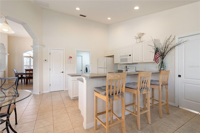 kitchen featuring arched walkways, light tile patterned floors, white appliances, visible vents, and white cabinetry