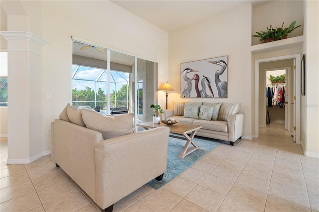 living area featuring a towering ceiling, a sunroom, baseboards, and light tile patterned flooring