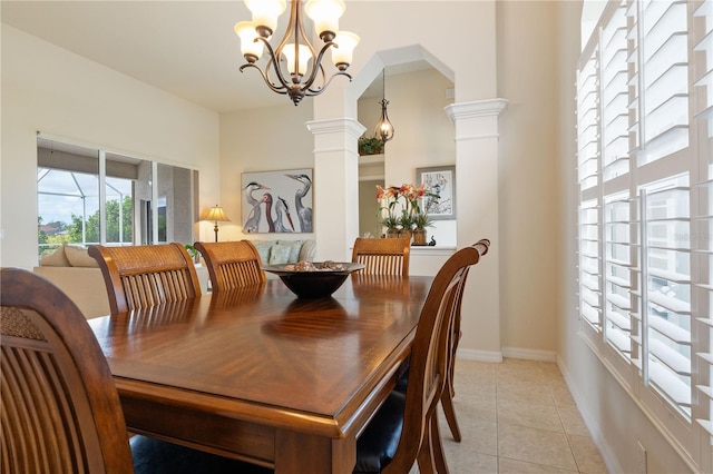 dining room featuring arched walkways, ornate columns, light tile patterned flooring, a chandelier, and baseboards