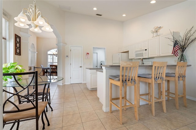 kitchen featuring hanging light fixtures, white appliances, arched walkways, and white cabinets