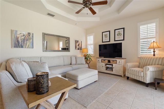 living room featuring light tile patterned floors, a tray ceiling, visible vents, and a ceiling fan