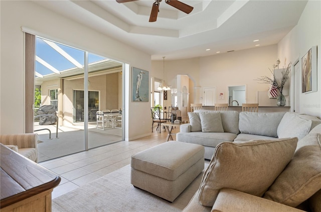 living area with light tile patterned floors, recessed lighting, a tray ceiling, and ceiling fan with notable chandelier