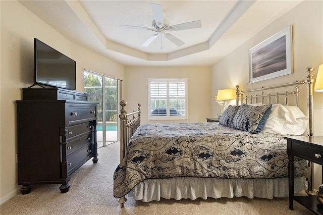 bedroom with access to exterior, a ceiling fan, a tray ceiling, and carpet flooring