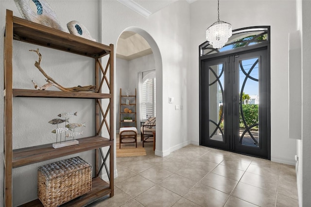 tiled entrance foyer featuring a notable chandelier, plenty of natural light, crown molding, and french doors