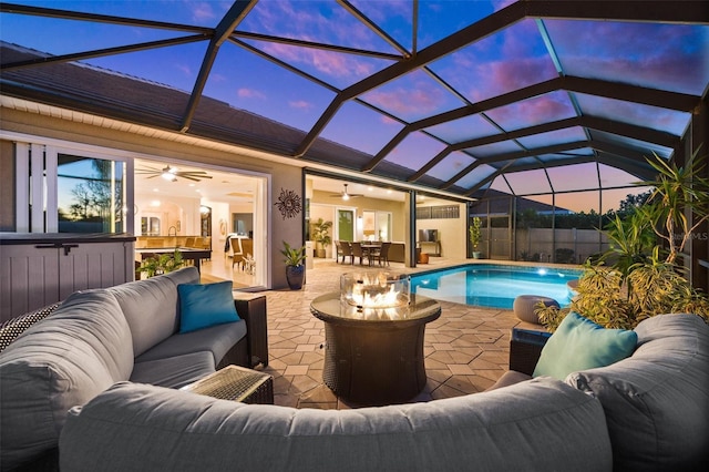 pool at dusk featuring an outdoor living space, ceiling fan, a patio, and glass enclosure