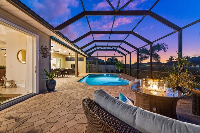 pool at dusk featuring an outdoor living space, a patio area, ceiling fan, and a lanai