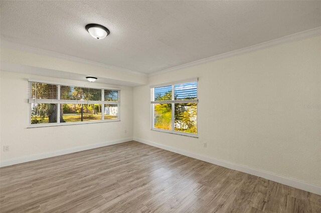 unfurnished room with light wood finished floors, a textured ceiling, baseboards, and crown molding