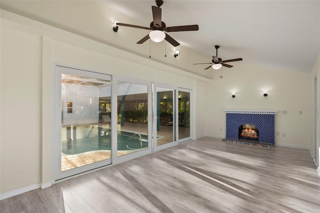 unfurnished living room featuring light wood-type flooring, baseboards, vaulted ceiling, and a tiled fireplace