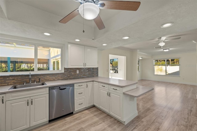 kitchen featuring white cabinets, dishwasher, backsplash, a peninsula, and a sink