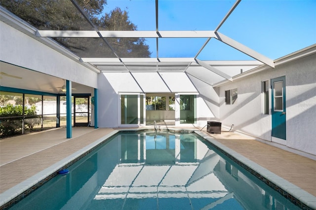 outdoor pool with glass enclosure, a patio area, and a ceiling fan