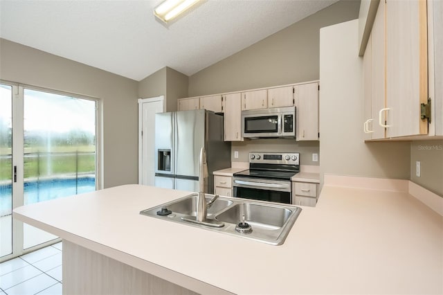 kitchen with lofted ceiling, light tile patterned floors, a textured ceiling, appliances with stainless steel finishes, and kitchen peninsula