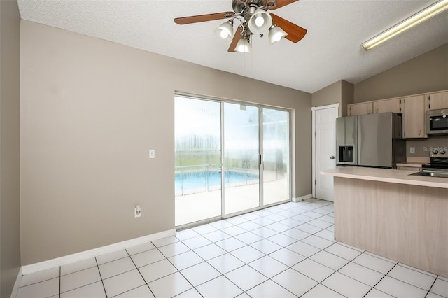 kitchen with appliances with stainless steel finishes, a textured ceiling, light brown cabinets, light tile patterned floors, and lofted ceiling