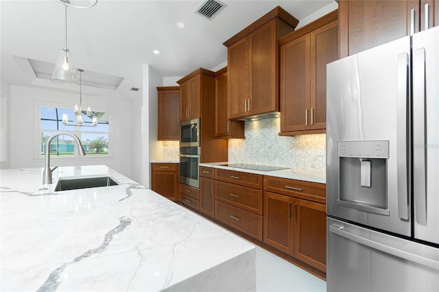 kitchen featuring sink, hanging light fixtures, appliances with stainless steel finishes, a raised ceiling, and light stone countertops